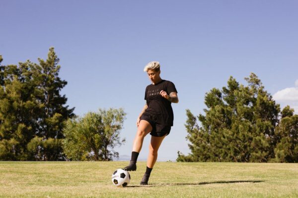 A woman playing soccer on a grass field under a clear sky, showcasing energy and focus.