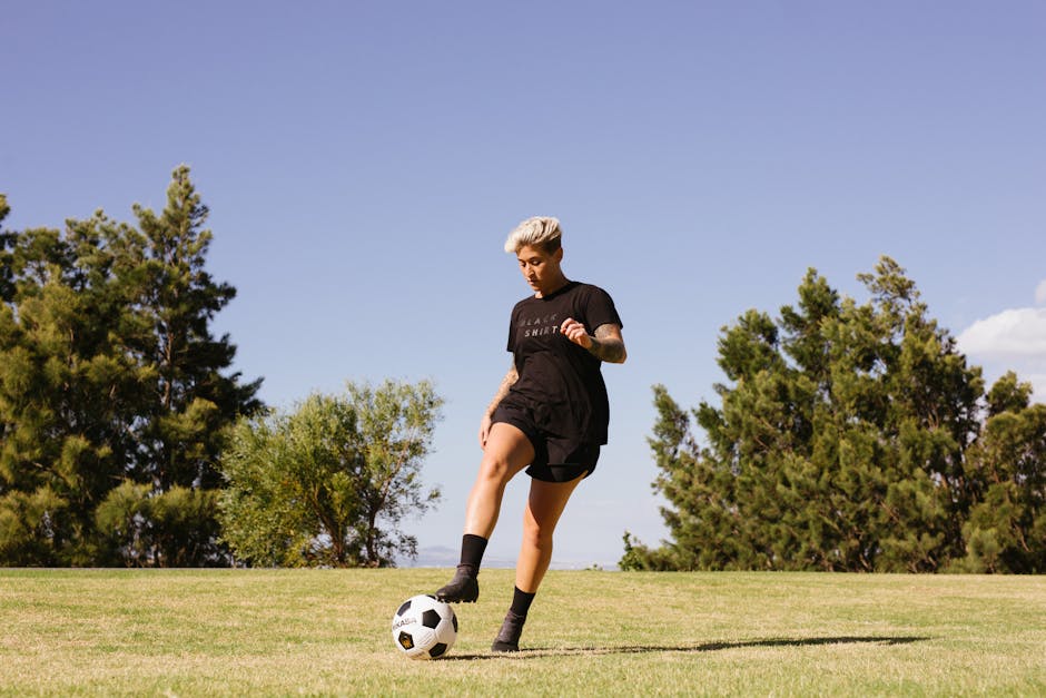 A woman playing soccer on a grass field under a clear sky, showcasing energy and focus.