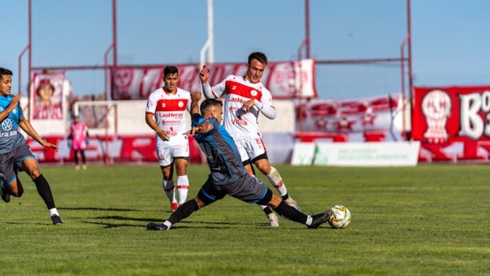 Competitive football match with players in action on a bright sunny day.